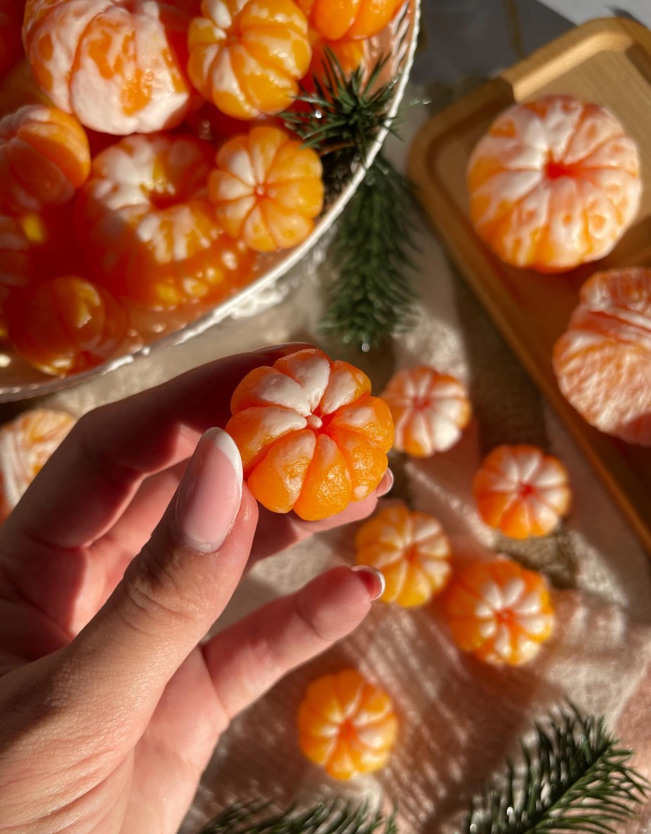 Small peeled-mandarin-shaped orange soaps held in a hand with fir sprigs