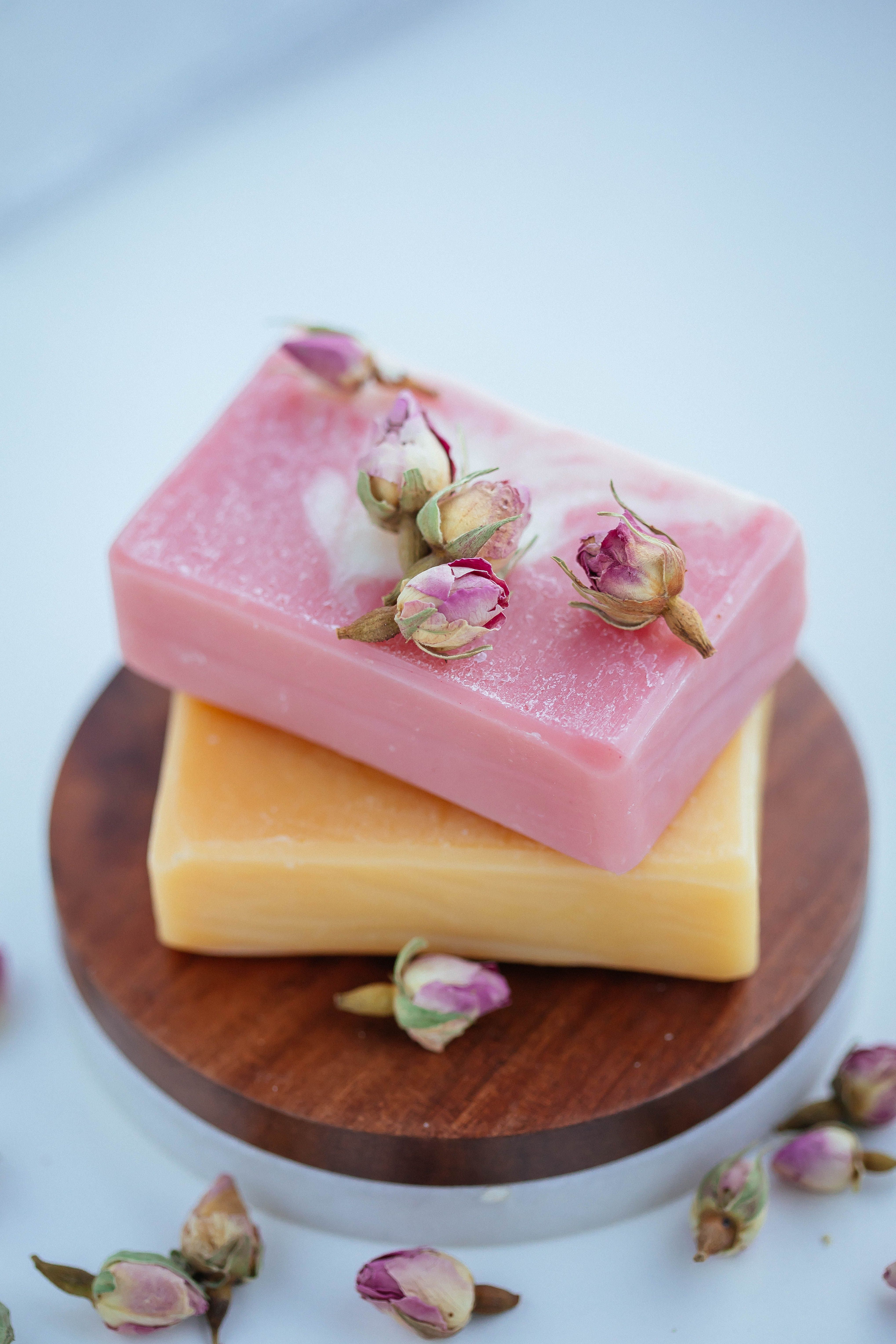 Pink rose soap bar with dried rosebuds stacked on an orange calendula bar on a wooden board